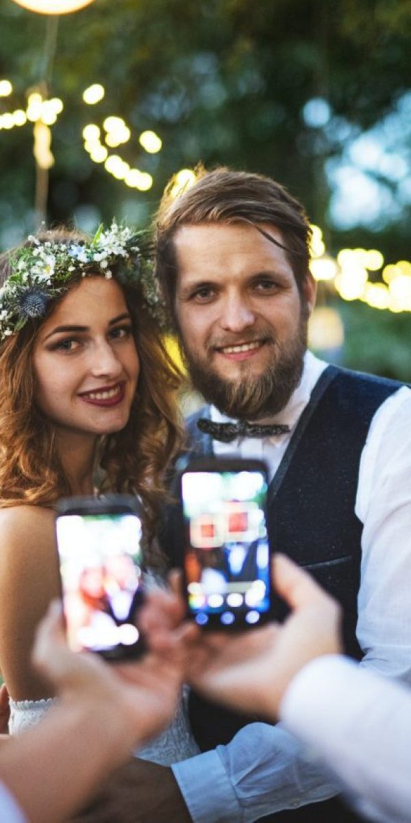 guests-with-smartphones-taking-photo-of-bride-and-groom-at-wedding-reception-outside-.jpg